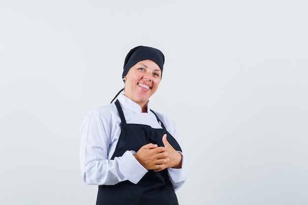 Blonde woman rubbing hands in black cook uniform and looking pretty , front view.