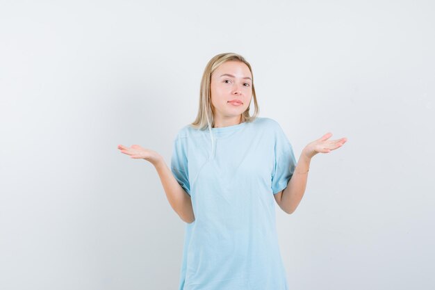 Blonde woman showing helpless gesture in blue t-shirt and looking confused