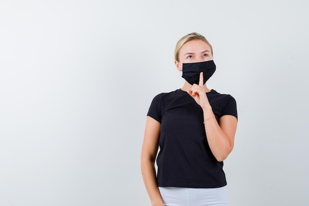 Blonde woman showing silence gesture in black t-shirt, white pants