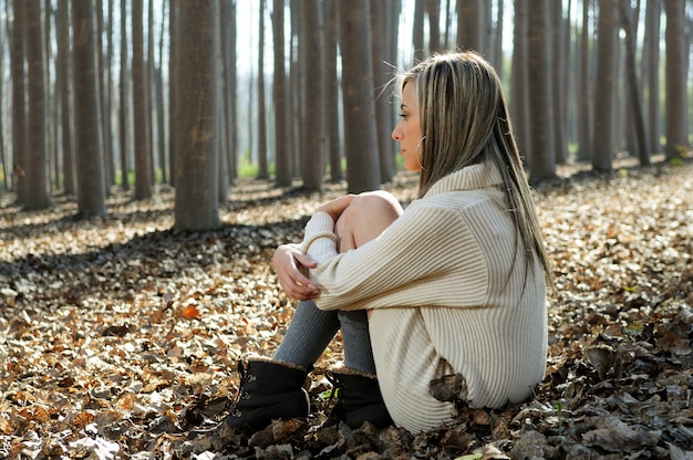 Free photo blonde woman sitting on leaves in a forest