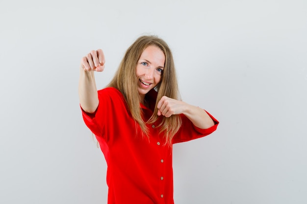 Blonde woman standing in fight pose in red shirt and looking confident ,