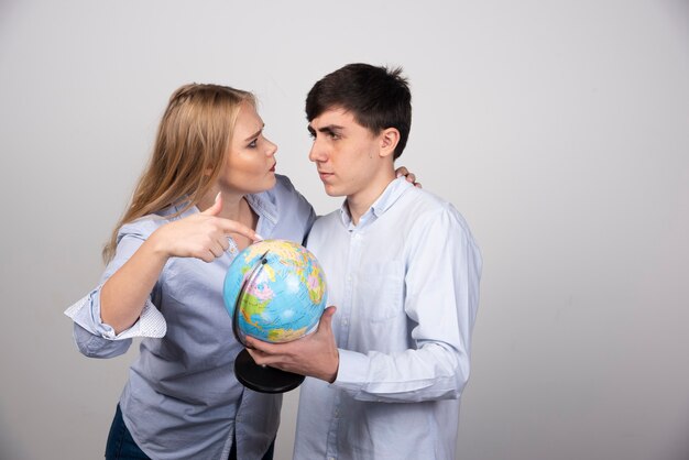 Blonde woman standing and pointing at earth globe near brunette guy