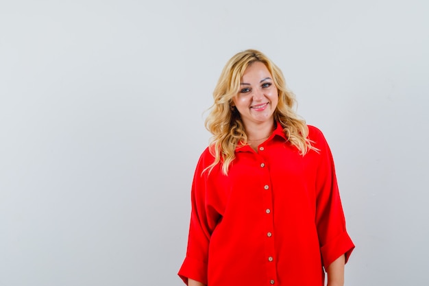 Free photo blonde woman standing straight and posing at camera in red blouse and looking happy