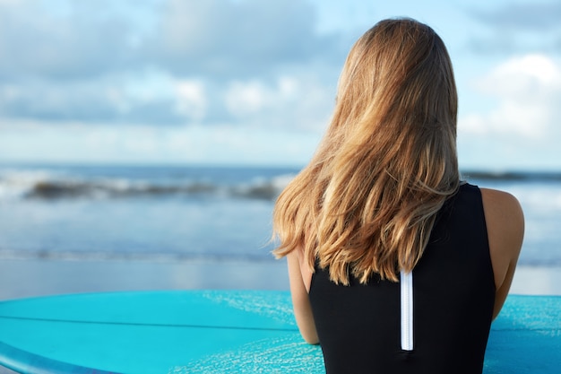 Blonde woman in swimsuit with surfboard on beach