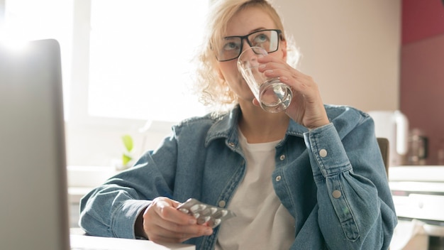 Free Photo blonde woman taking a pill near laptop