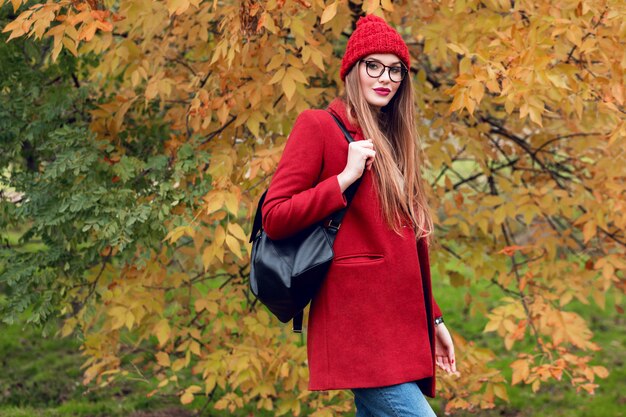 Blonde woman with long hairs walking in sunny autumn park in trendy casual outfit.