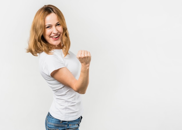 Blonde young woman clenching her fist standing against white background