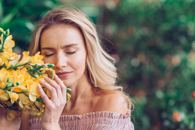 Free Photo blonde young woman closing her eyes touching the freesia flowers