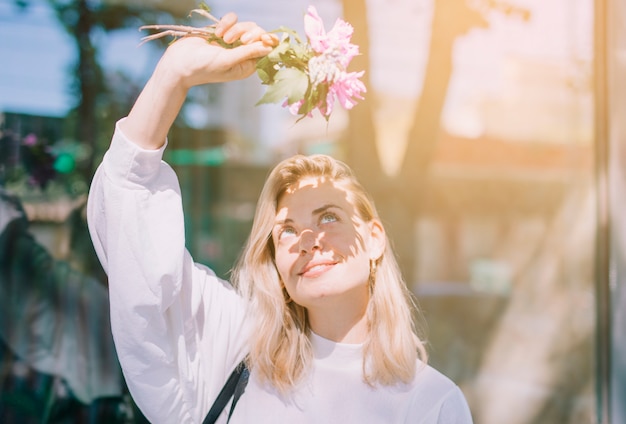 Free Photo blonde young woman holding flowers in hand shielding her eyes from the sunlight