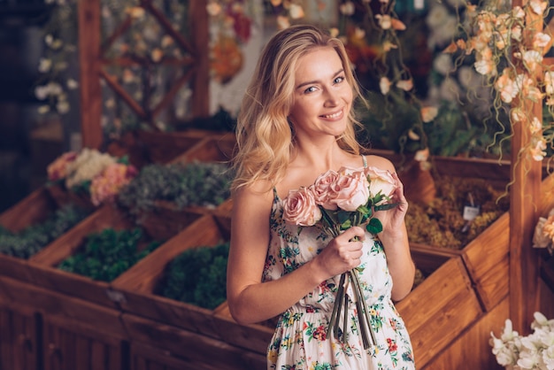 Blonde young woman holding pink roses in hand standing in florist shop