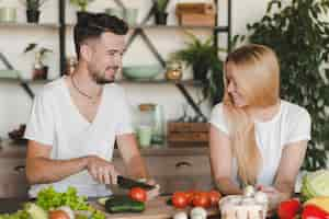 Free photo blonde young woman looking at man cutting vegetables with knife