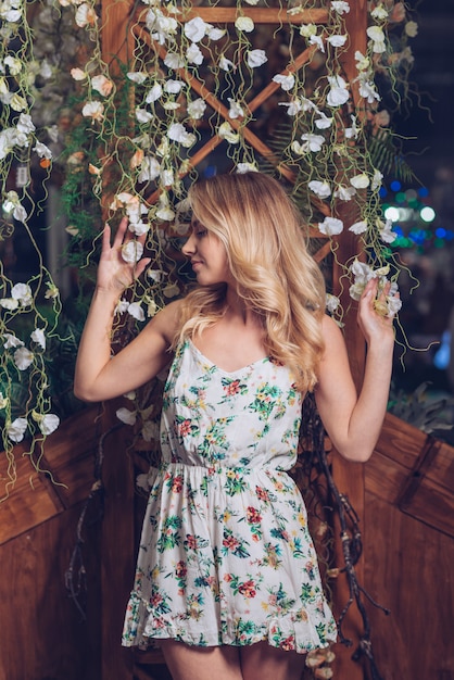 Free photo blonde young woman posing in front of flower decoration