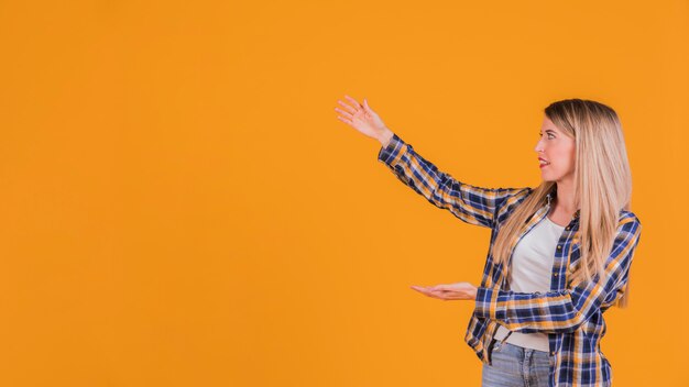 Blonde young woman presenting something against an orange background