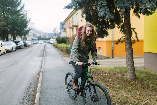 Free photo blonde young woman riding bicycle on road in the city