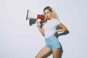 Free photo blonde young woman shouting with a megaphone isolated on a white wall