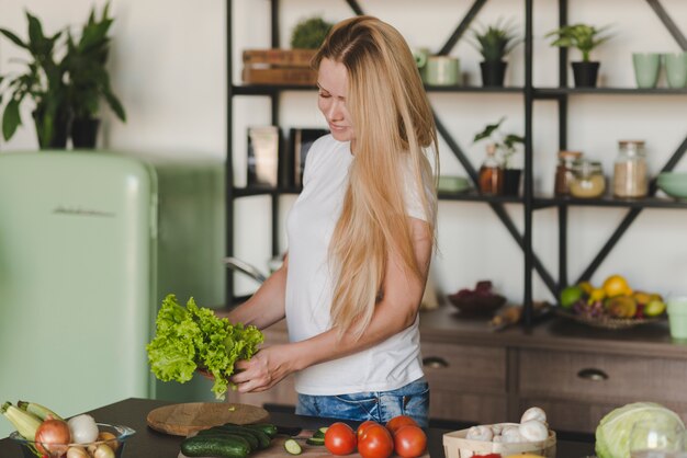 Blonde young woman standing in kitchen holding lettuce