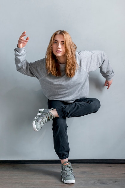 Free photo blonde young woman standing on one foot against grey wall