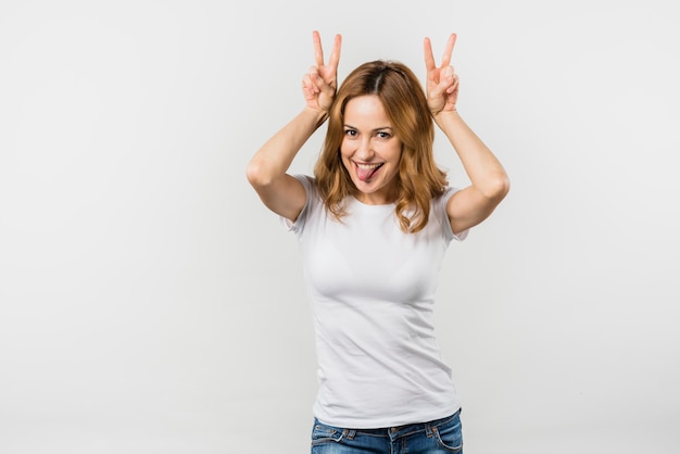 Blonde young woman sticking out her tongue making horn gesture