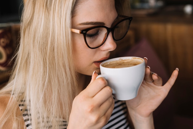 Blonde young woman wearing eyeglasses drinking coffee