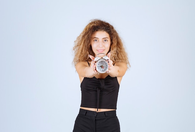 Free photo blondie girl holding and promoting an alarm clock.