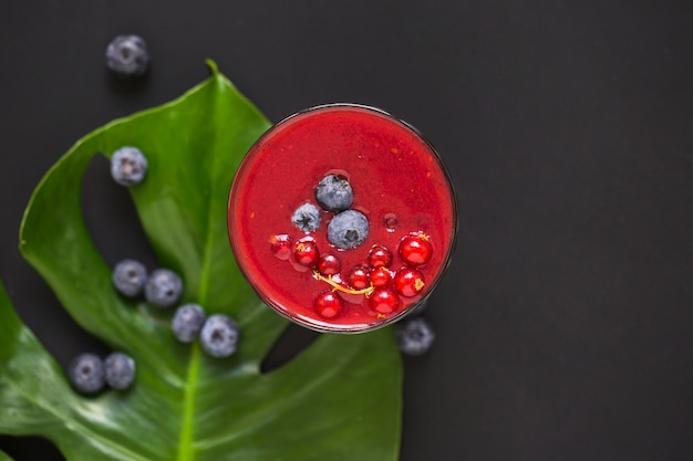 Blue berries on smoothie and green leaf against black background