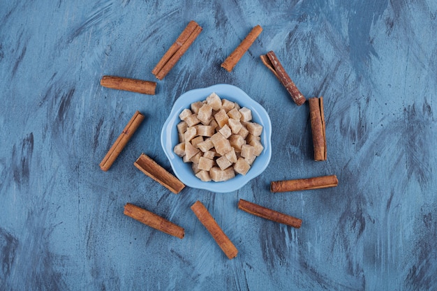 Free Photo blue bowl of brown sugar cubes and cinnamon sticks on blue surface. 