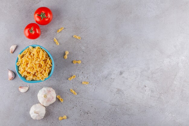 A blue bowl full of Farfalle raw dry pasta with vegetables on a stone table.