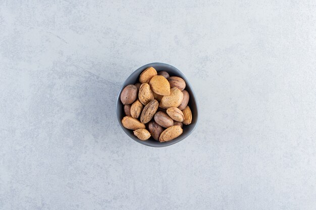 Blue bowl full of shelled almonds and walnuts on stone background.