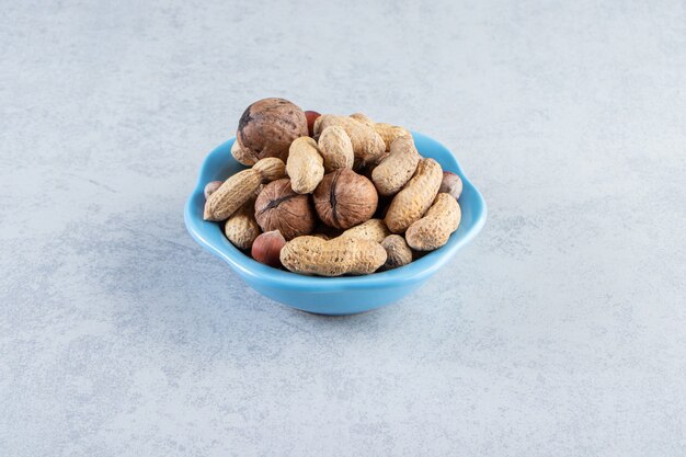 Blue bowl of organic nuts placed on stone background.