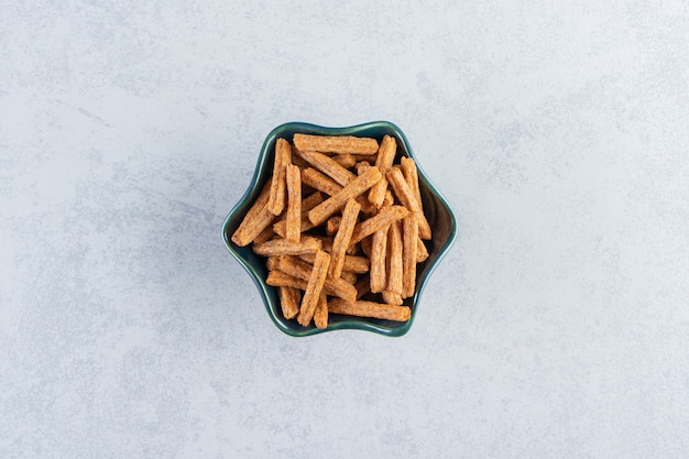 Free Photo blue bowl of tasty stick crackers on stone background.