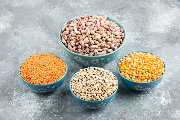 Blue bowls of various beans and corns on marble table.