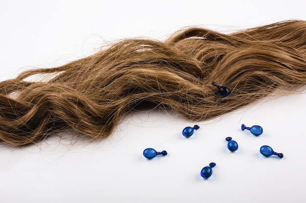 Free photo blue capsules with vitamins for hair lie on brown hair curls