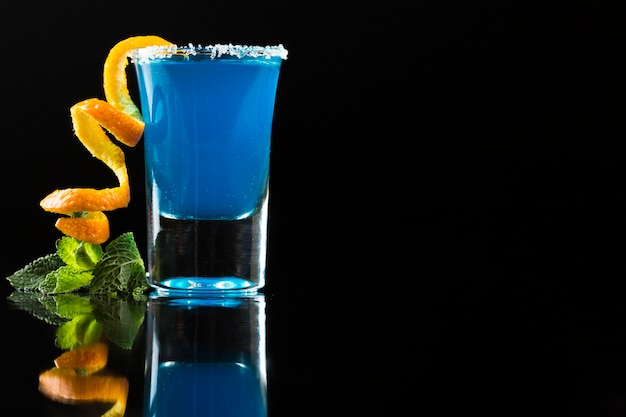 Free photo blue cocktail in shot glass with orange peel and mint