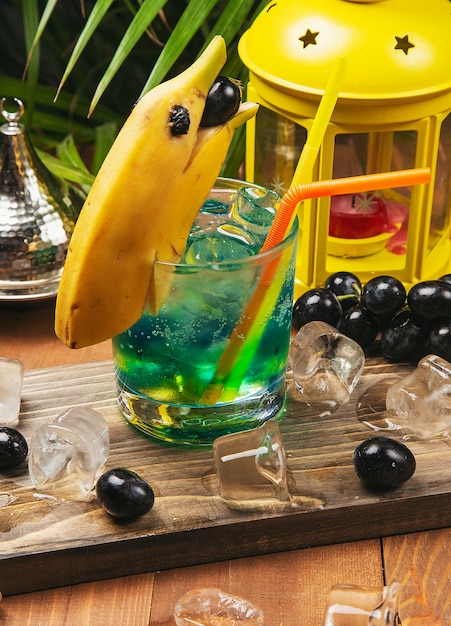 Blue cocktail with banana dolphin decoration, black grapes on a wooden board 