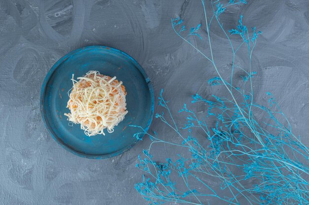 Blue decorative branches next to a platter of cheese-topped portion of cooked rice on marble table.