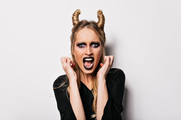 Blue-eyed european woman posing in witch costume with unpleased face expression. angry blonde vampire with black makeup.