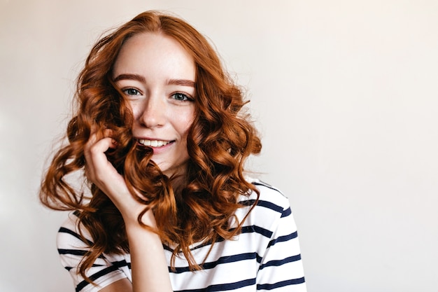 Blue-eyed ginger girl posing with happy smile. Indoor shot of amazing red-haired lady isolated.