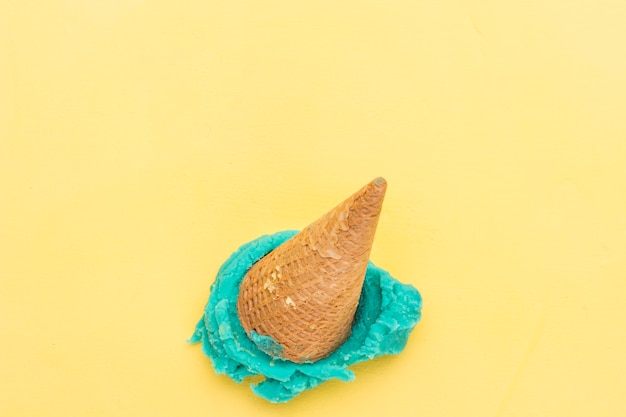 Free photo blue ice cream in cone falling on yellow background