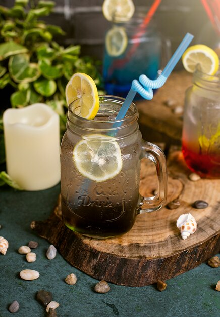 Blue lagoon, red and brown cocktail with lemon slices inside jar with stick   