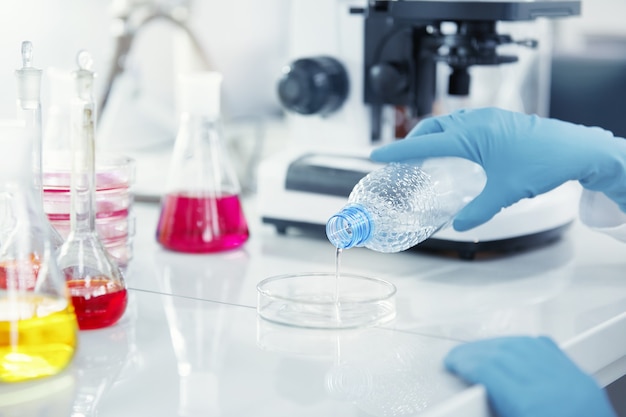 Blue latex gloves holding plastic bottle and pouring transparent liquid