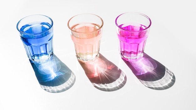 Free photo blue; pink and red liquid glasses with shiny dark shadow on white backdrop