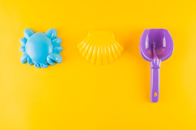 Free photo blue plastic scallop seashell; crab and plastic shovel on yellow background