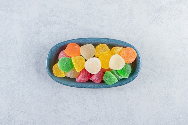 Blue plate of colorful jelly marmalades on marble background.