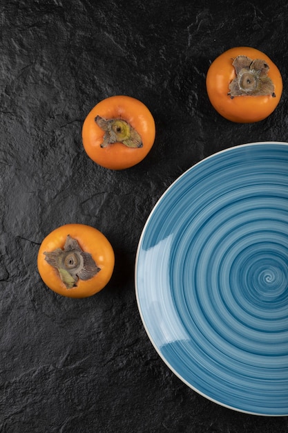 Blue plate of delicious ripe fuyu persimmons on black surface