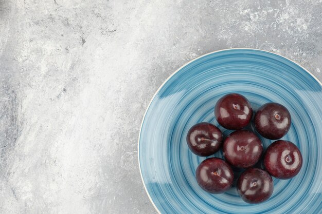 Free Photo blue plate of fresh purple plums on marble surface.