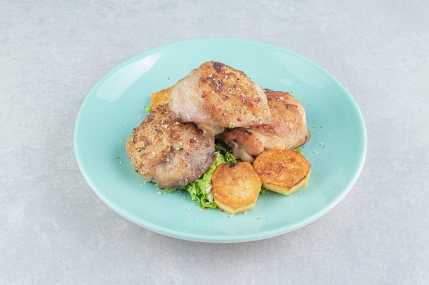 A blue plate of meat with fried sliced potatoes and lettuce. 