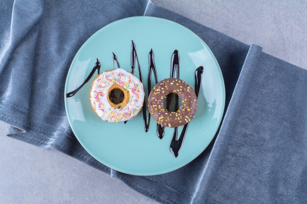 A blue plate of two sweet doughnuts with colorful sprinkles. 