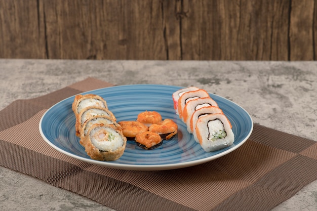 Blue plate of various sushi rolls on marble table