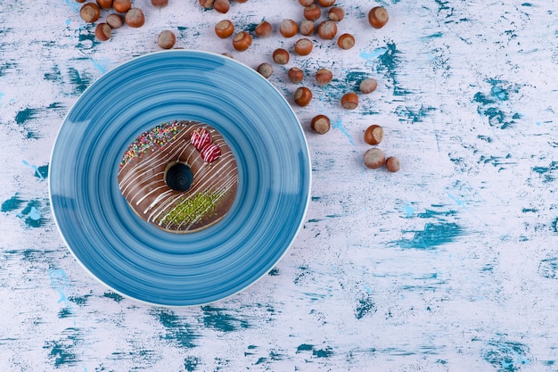 Blue plate with chocolate donut and shelled hazelnuts on white surface.