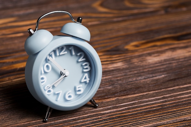 Blue small alarm clock on wooden textured backdrop